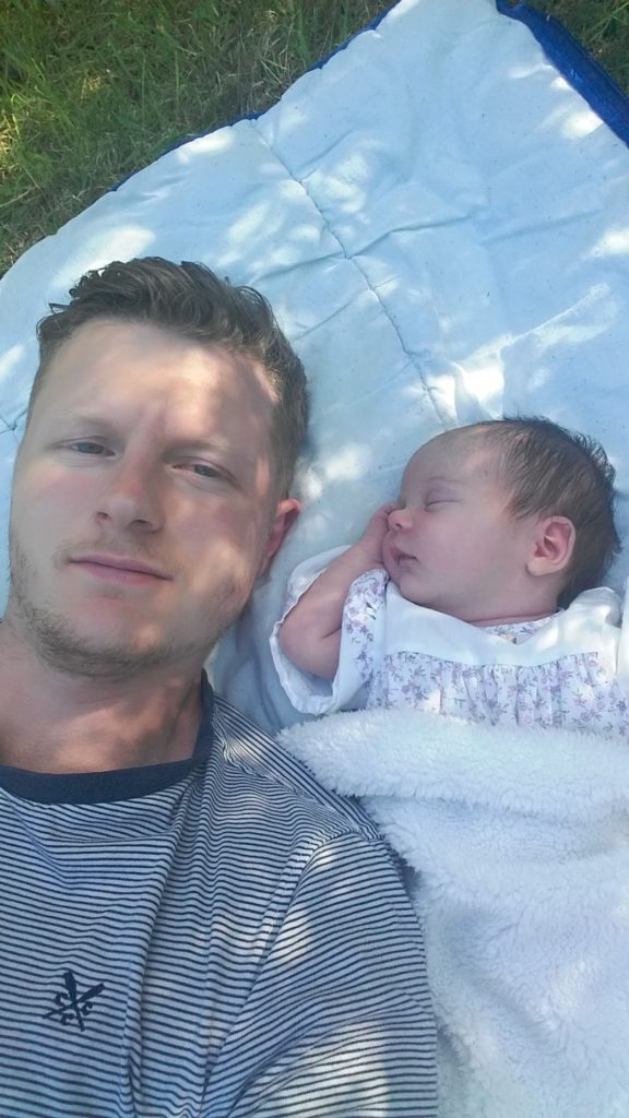 Man and his newborn daughter lay on a blanket in the shade.