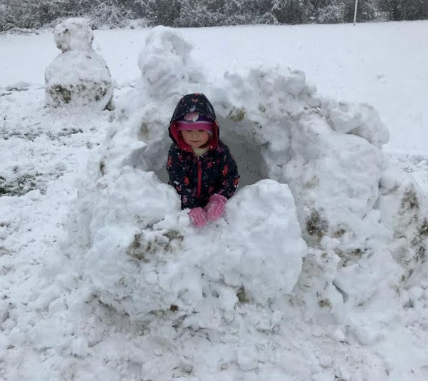 A little girl building an igloo in a snowy field.