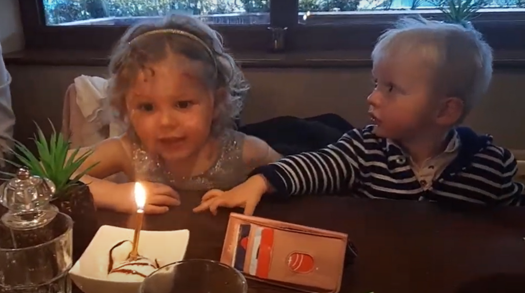 A young girl is about to blow out a birthday candle as her little brother looks on