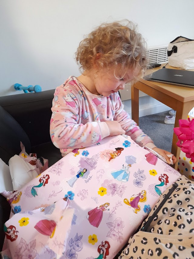 A young girl in pyjamas opens birthday presents.