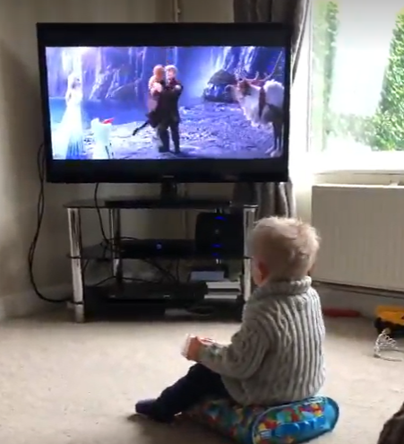 A boy sat on the living room carpet watching Frozen on the television