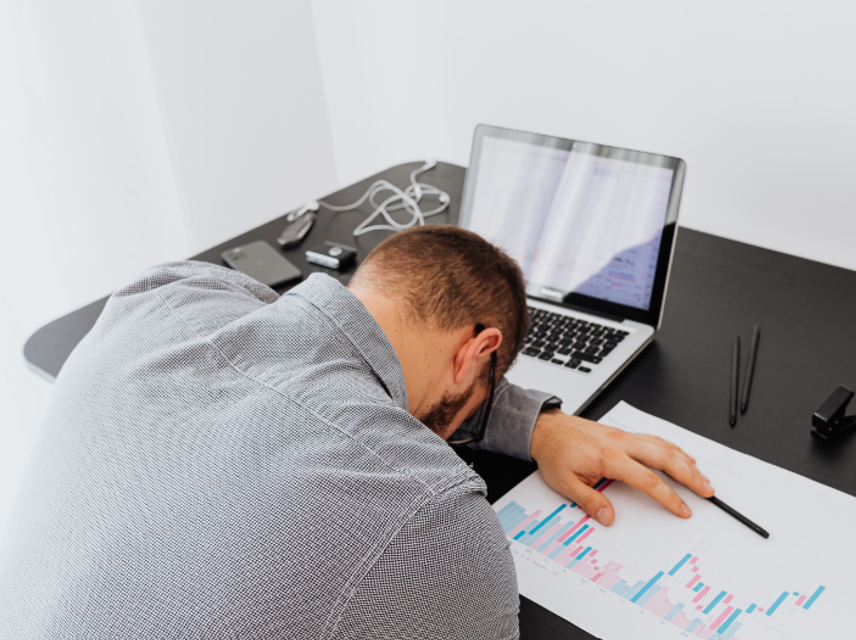 A man slumps on his desk, exhausted from work.