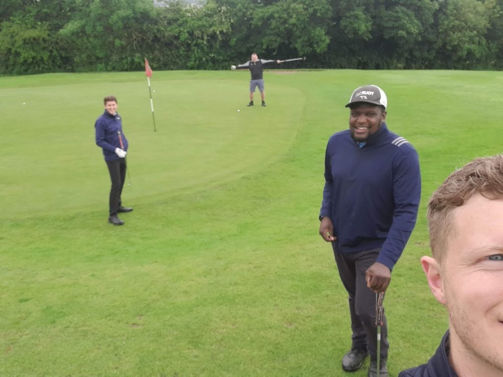 Four men standing around a putting green, smiling because they all hit good shots.