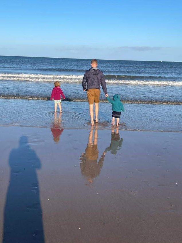 A man and his young son and daughter paddle in the sea. 