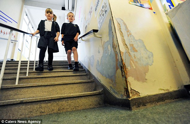 Some schoolchildren walk down a stairwell with crumbling, peeling walls.